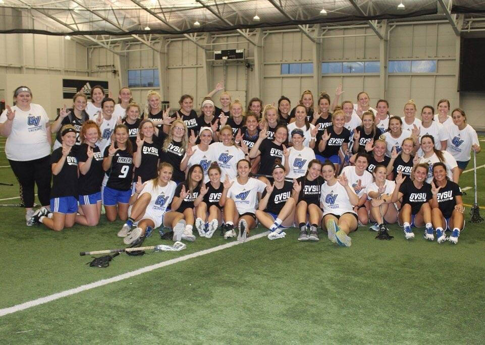 Large group of women in GVSU Lacrosse shirts on an indoor lacrosse field
